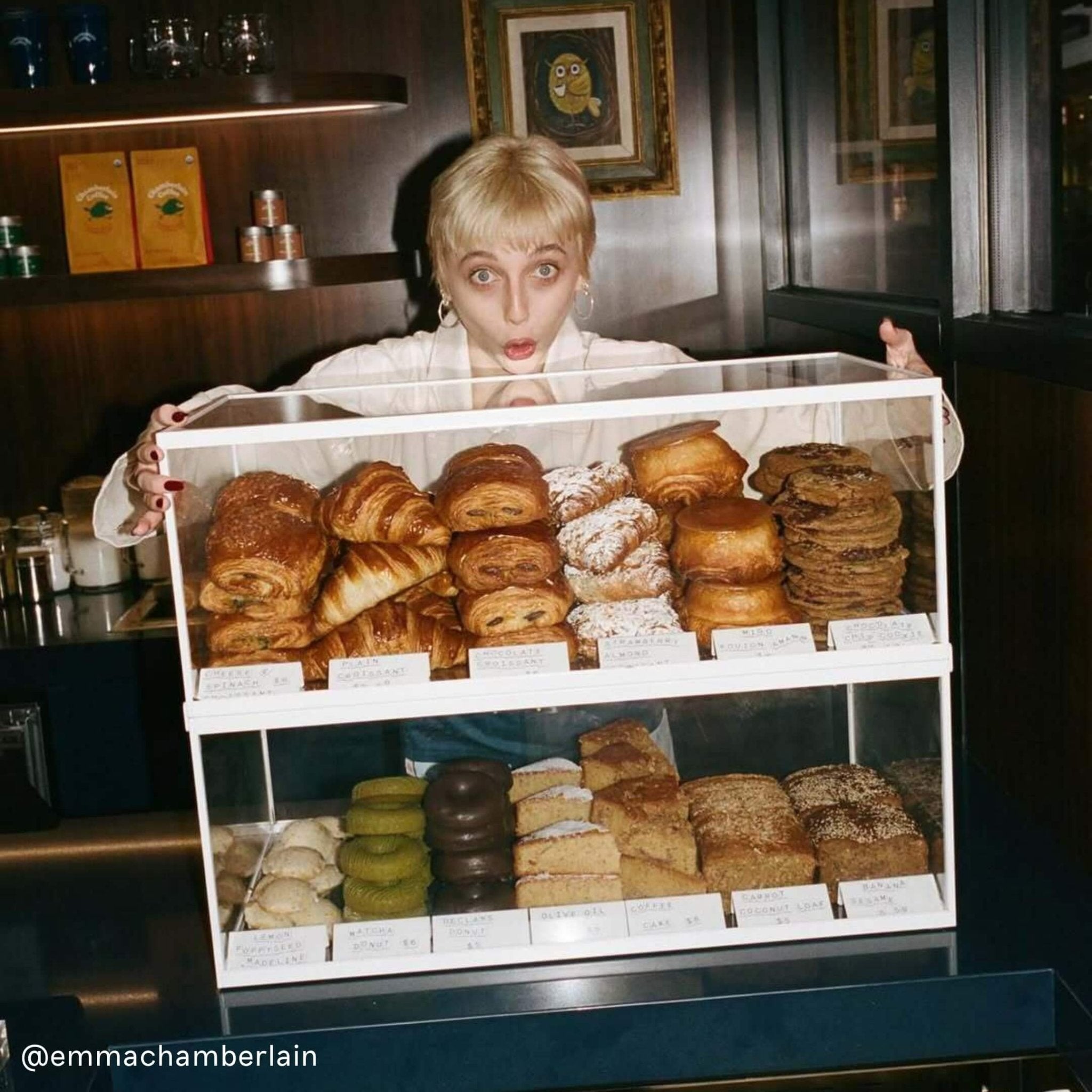 Stacked white bakery display cabinet filled with croissants in busy café window full of baked goods
