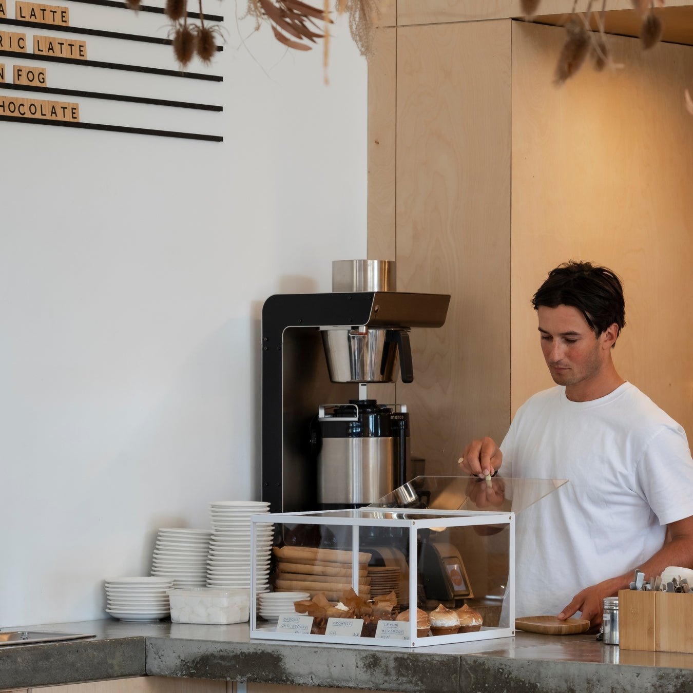 Barista behind acrylic bakery display case filled with pastries in coffee shop