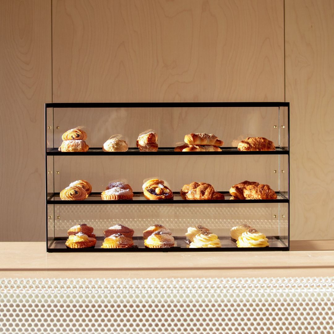 black three-tier pastry acrylic display case with pastries inside sitting on countertop