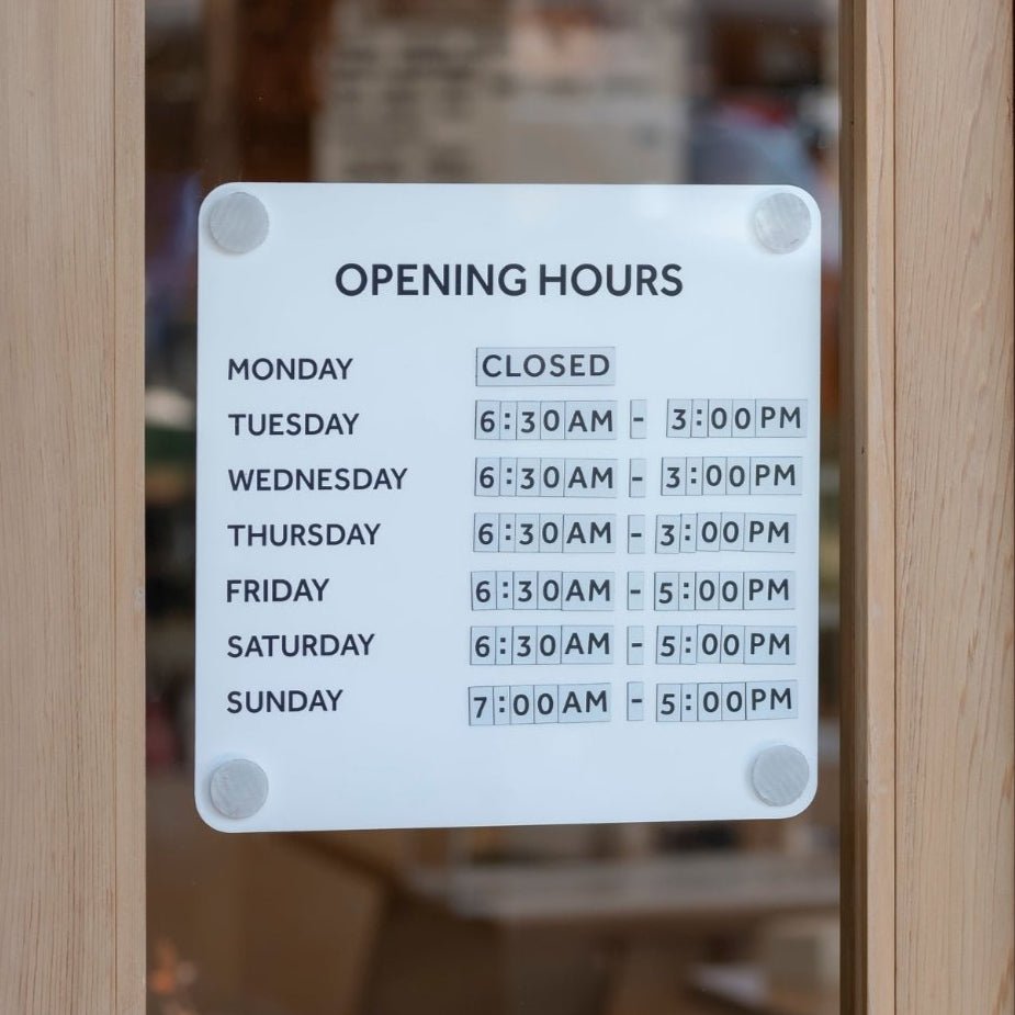business hours of operation sign mounted on glass door showing business hours in white steel panel
