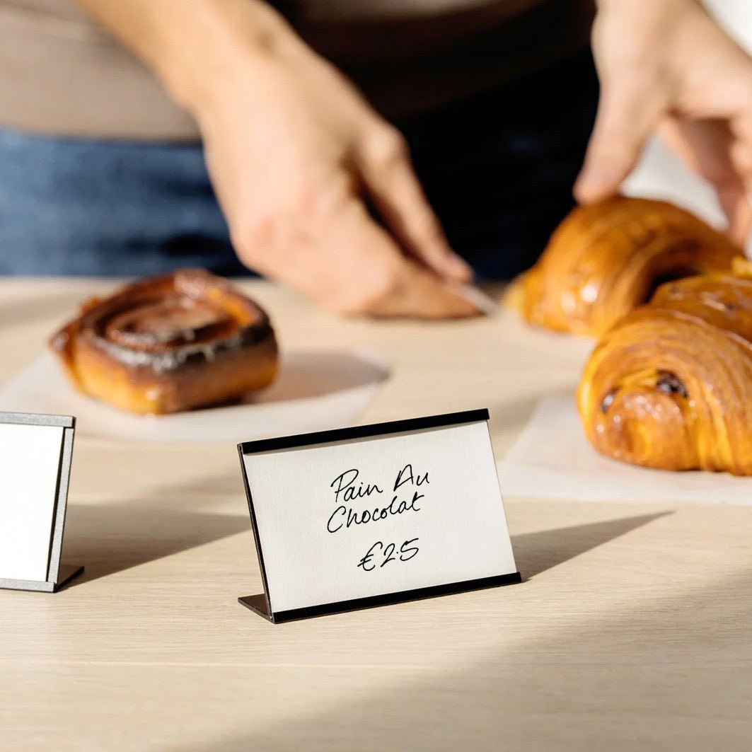 brass card counter sign frame with pastry price on a counter top with pastries behind it