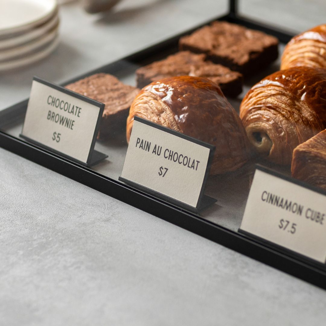 card counter signs in front of scones and banana bread showing names and prices
