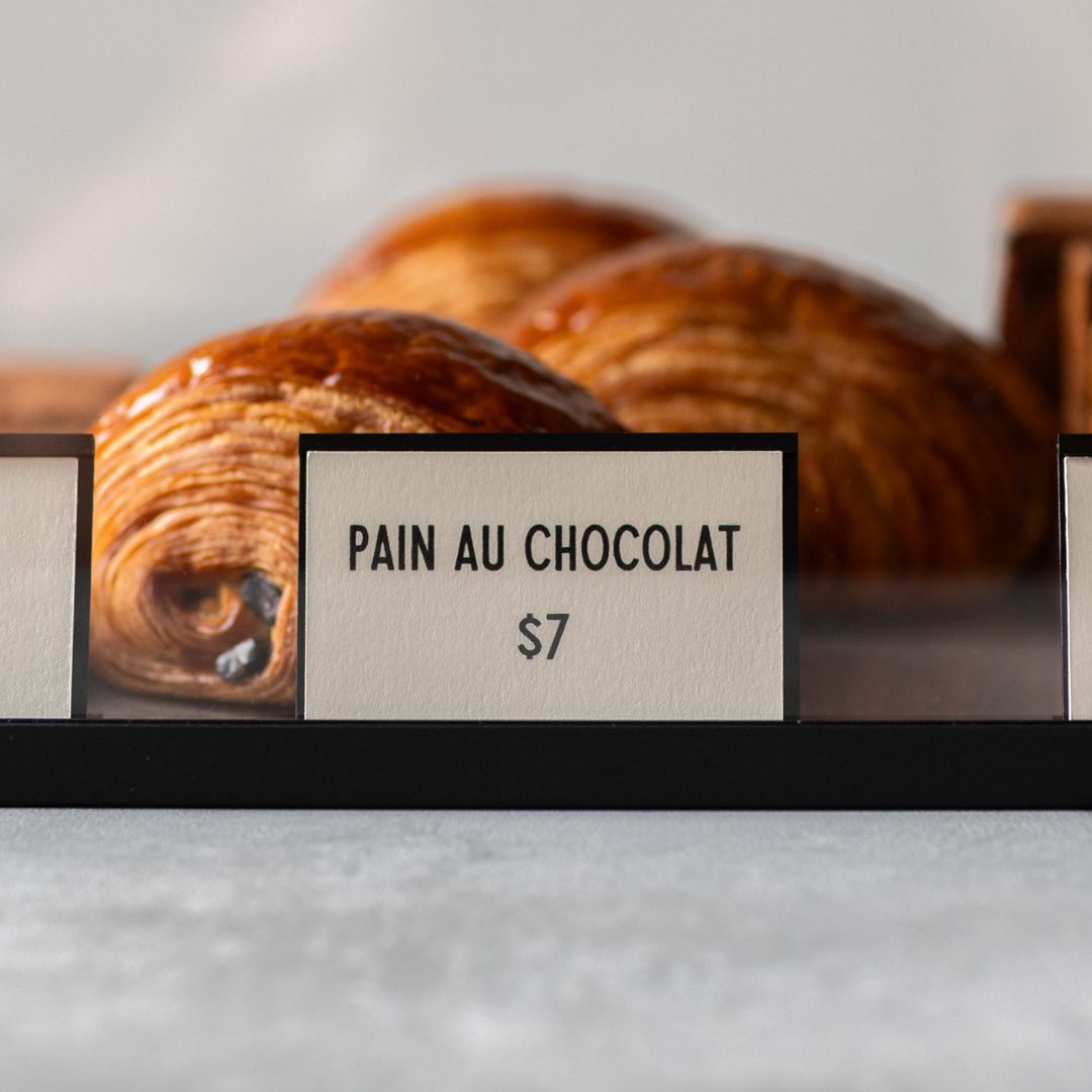 card counter signs in front of pan au chocolat pastries showing names and prices