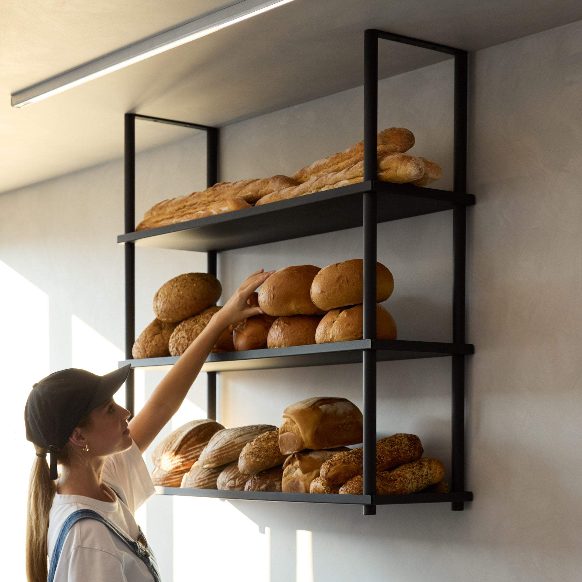 black ceiling mounted shelves displaying bread at a bakery with girl reaching up to grab a loaf