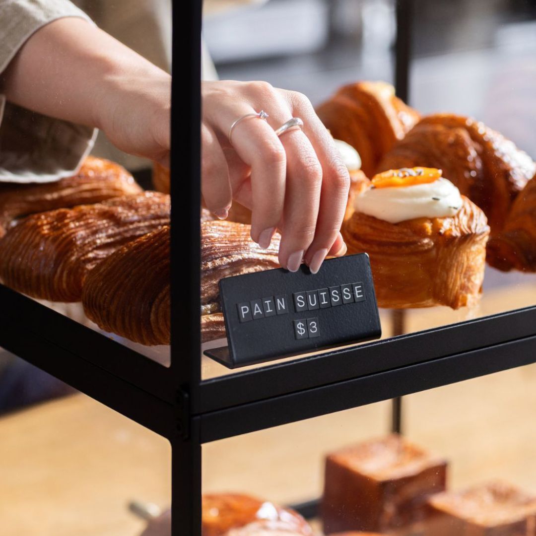 bakery display case with small black magnetic counter signs inside next to pastries