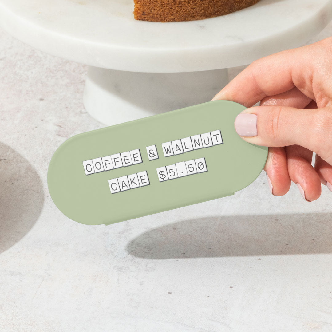 hand holding up a green curve counter sign that has pastry display pricing on it