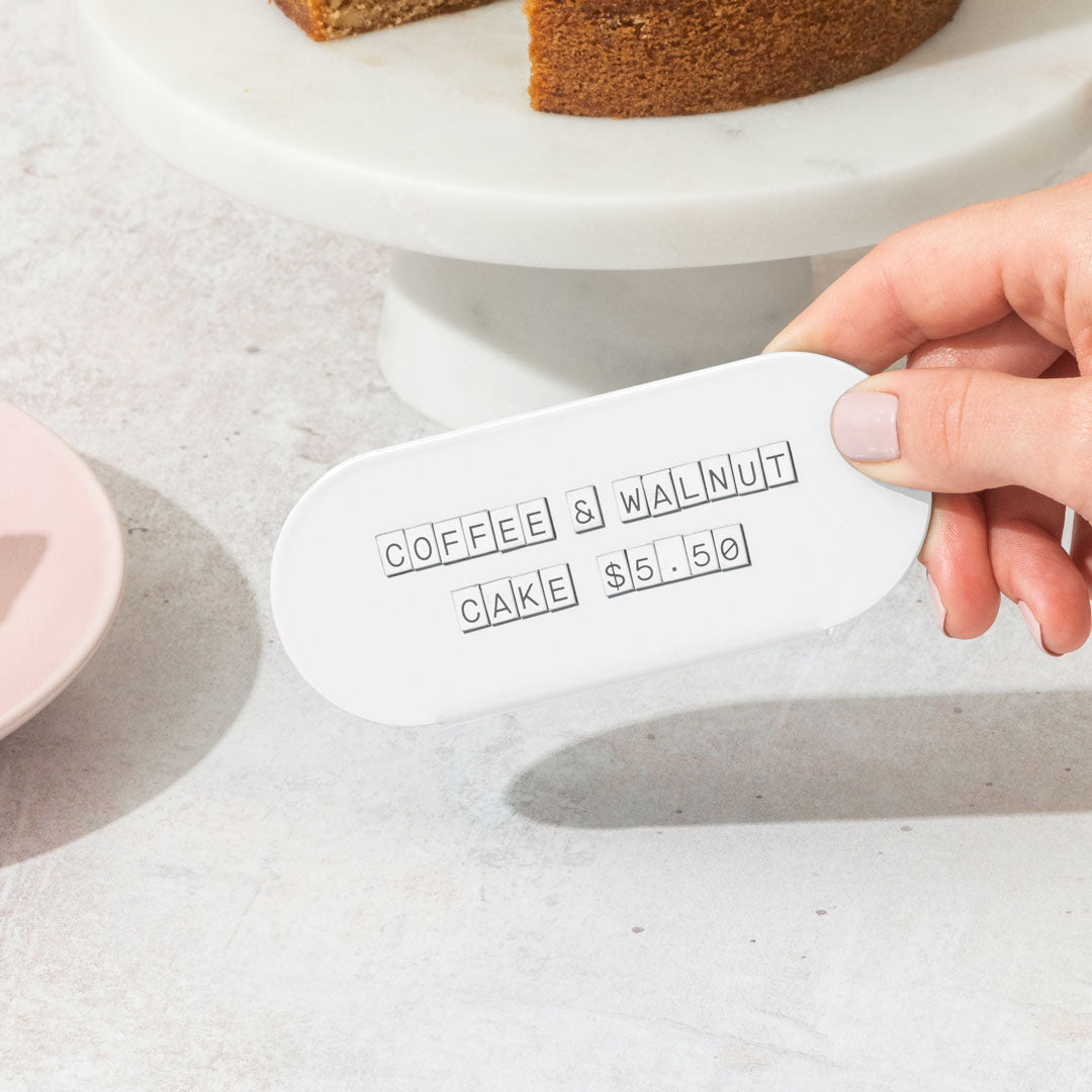 hand holding up a white curve counter sign that has pastry display pricing on it