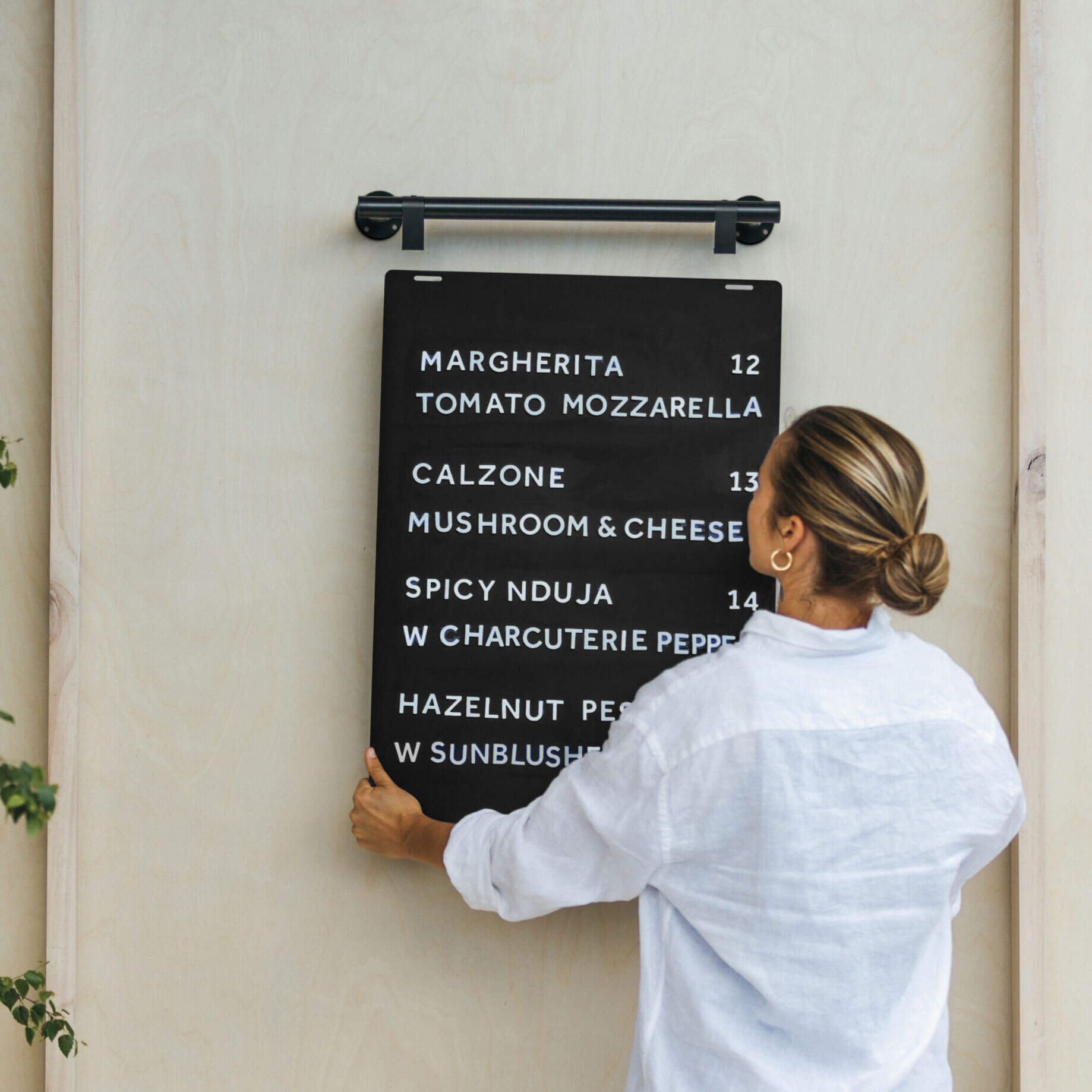 person lifting a black hanging menu board onto the hooks mounted on the wall