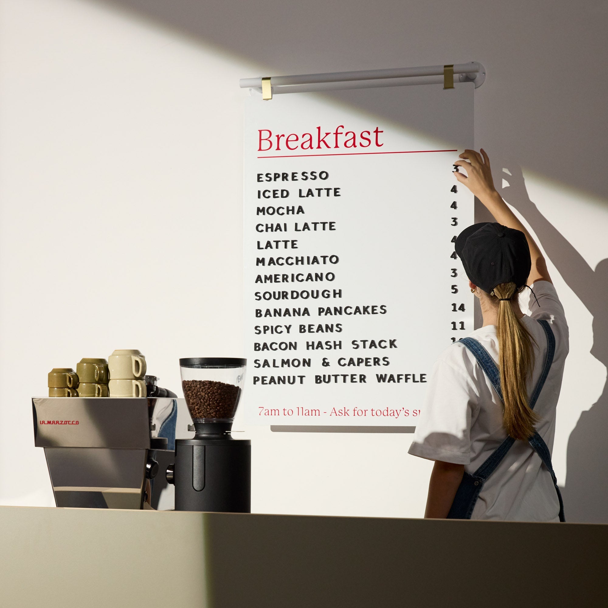 person holding the side of a large hanging menu board behind a cafe countertop to show size to scale