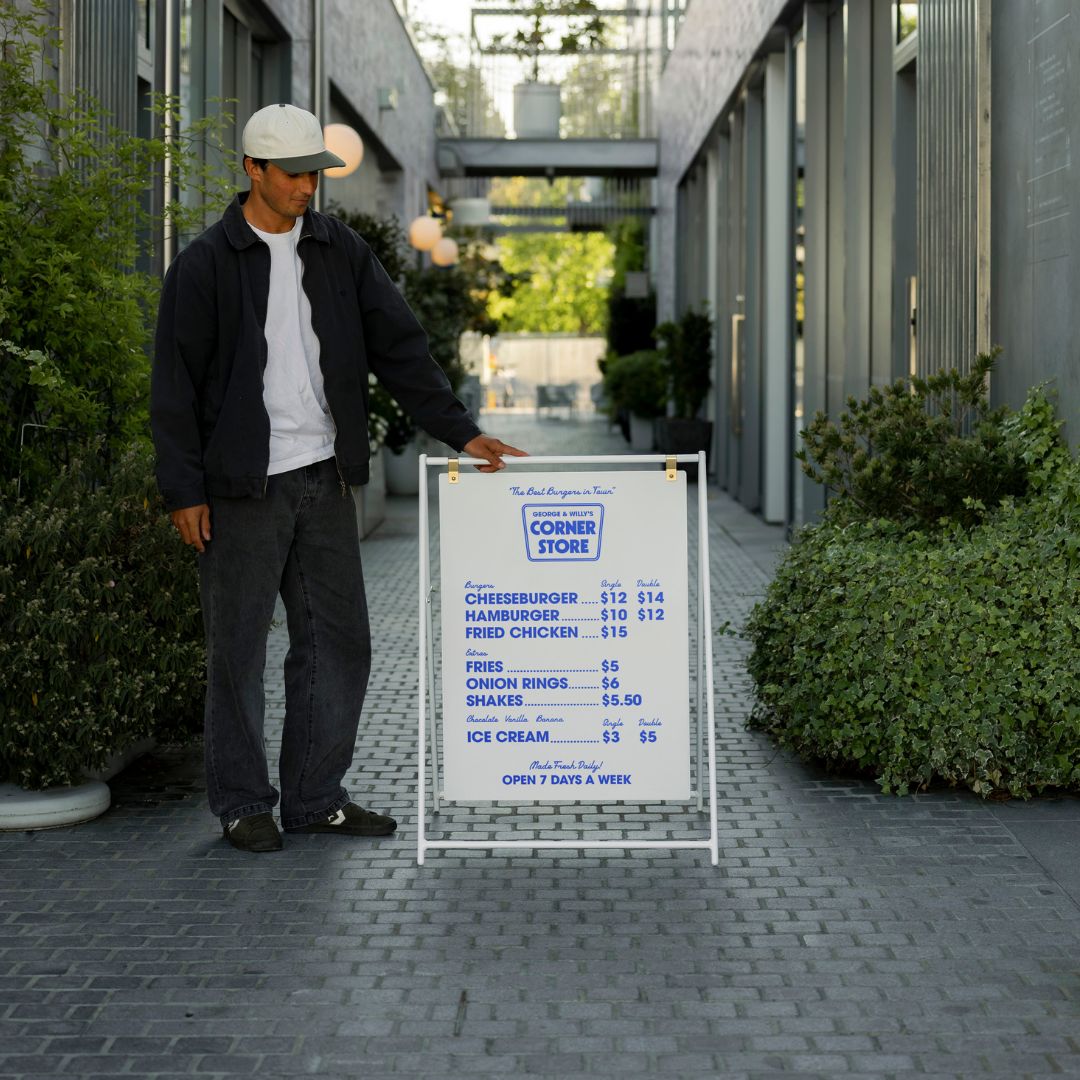 white large sidewalk pavement sign in an alleyway with a person standing beside it