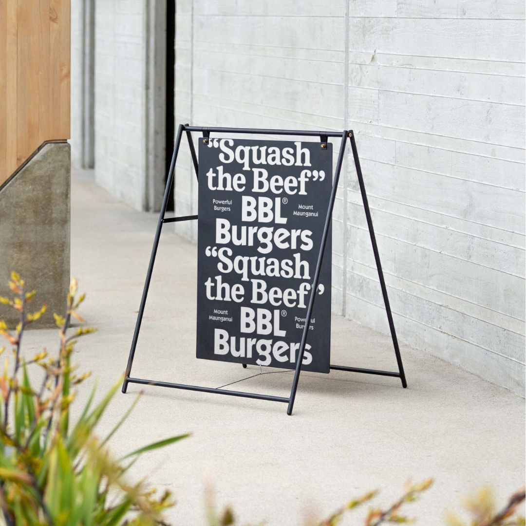 black large sidewalk sign outside on a sidewalk against a concrete building