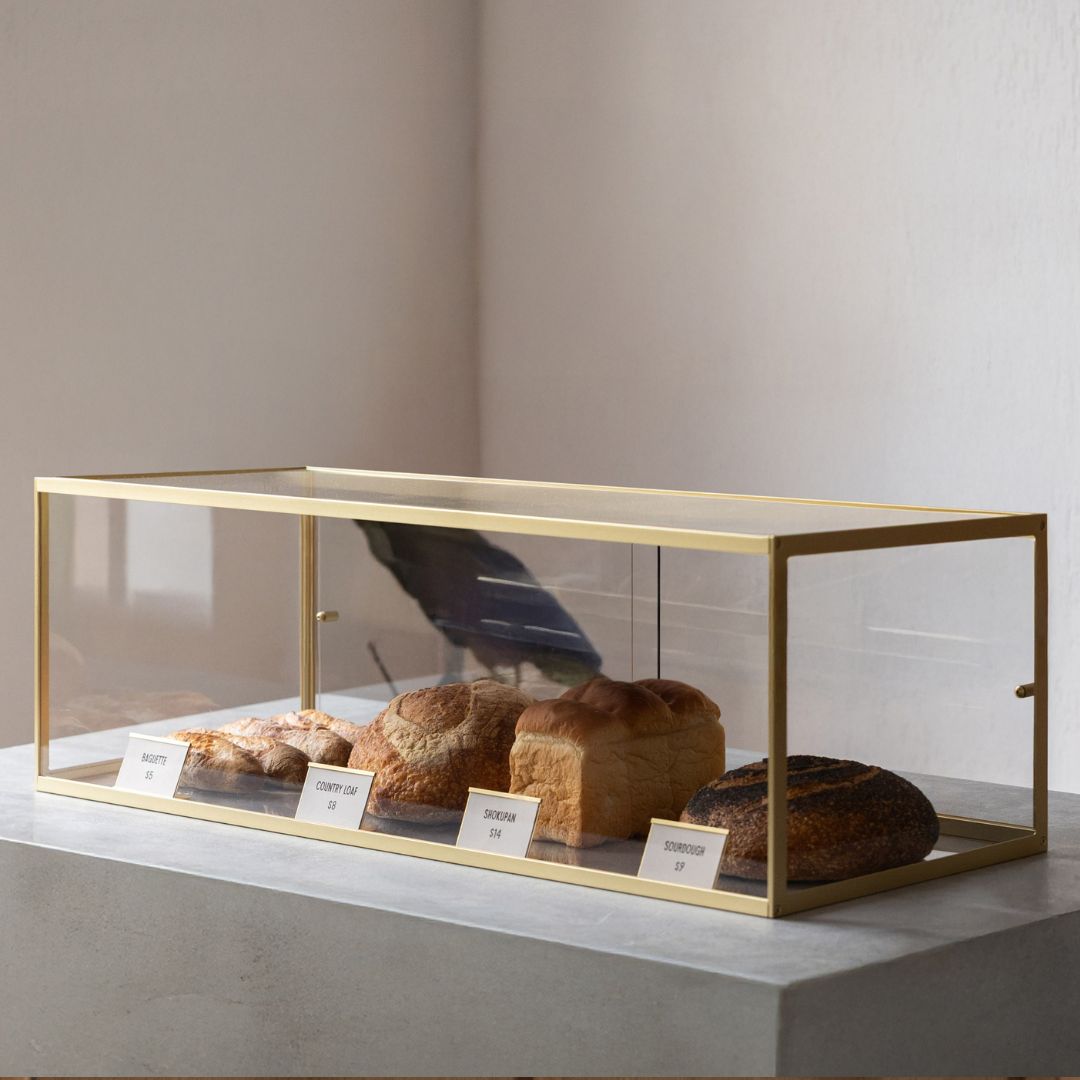 Modern brass and acrylic bakery display case on café counter with croissants displayed