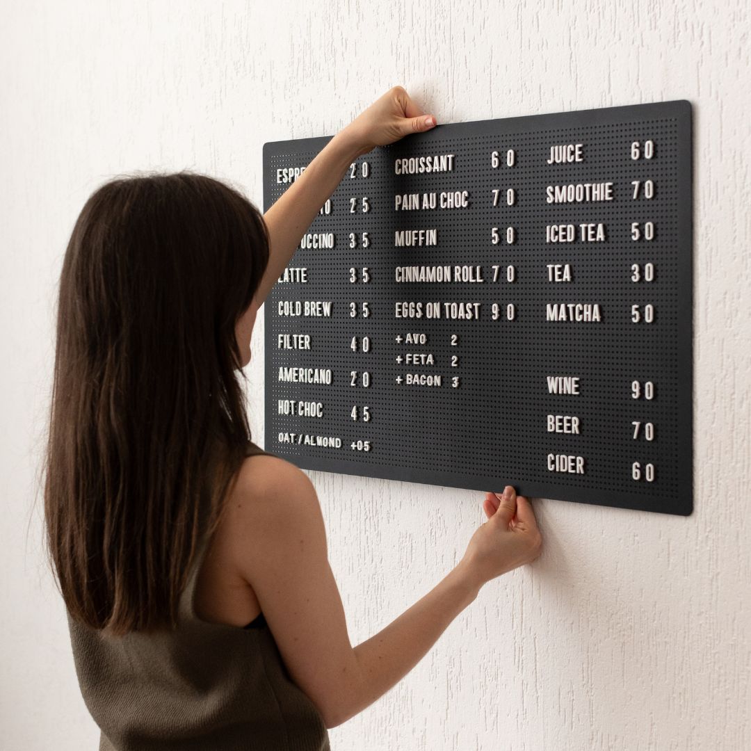 Woman placing black peg letter board on magnetic wall mounts with café drinks menu