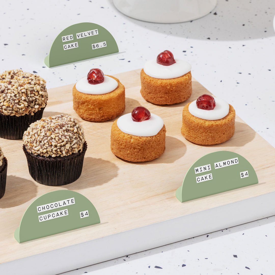 sage green round counter signs in front of mini cakes with white magnet letters