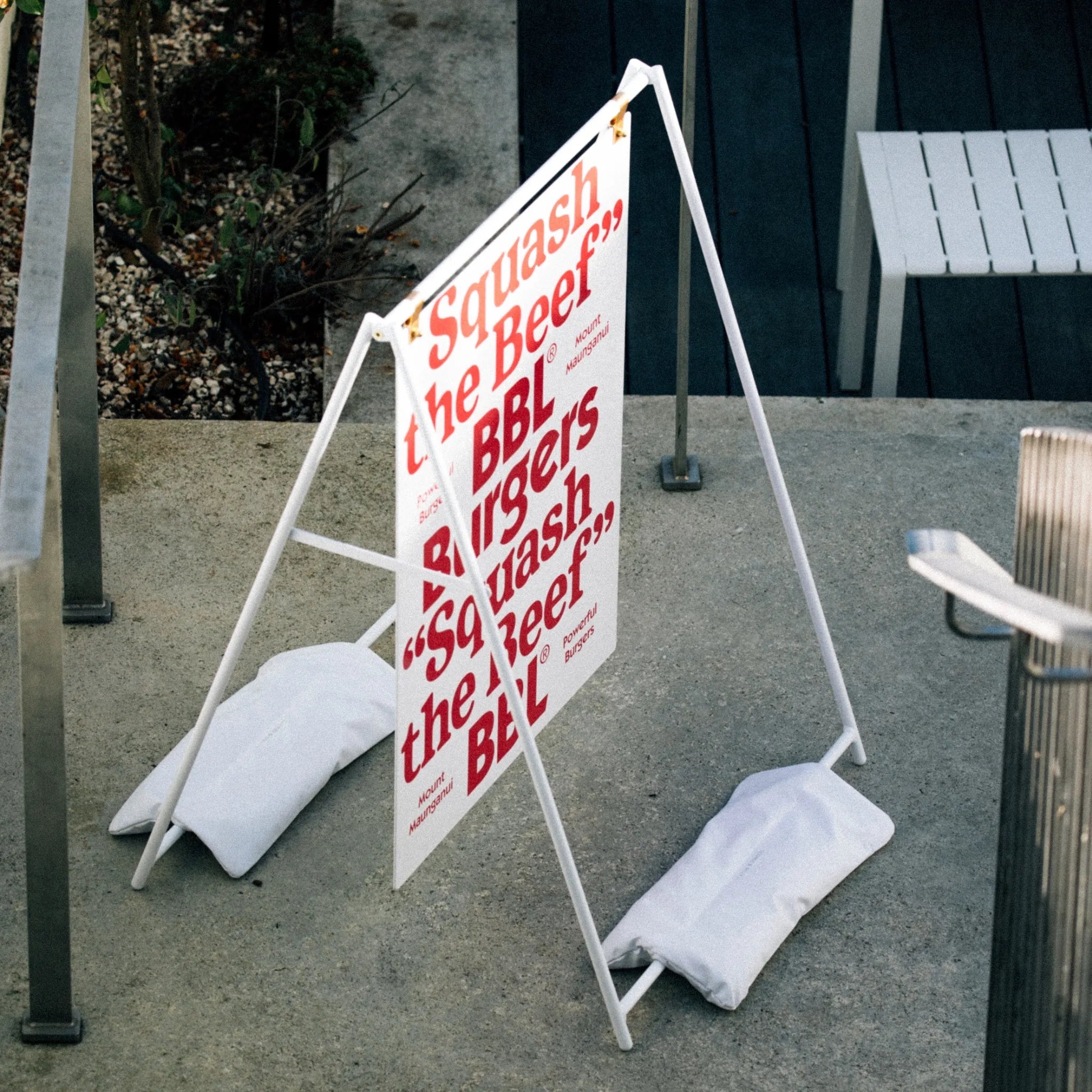 large a-frame sign with red logo on it using white sandbags