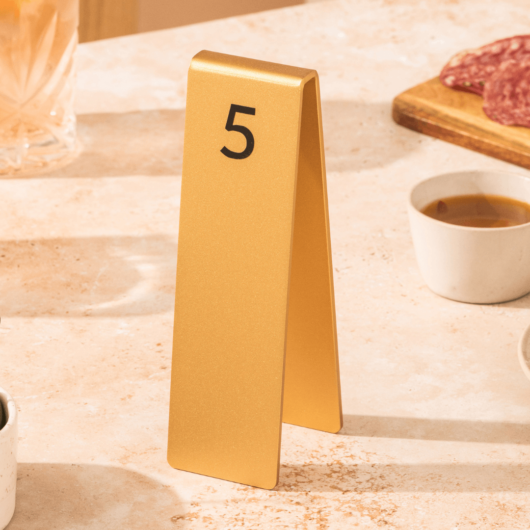 Gold aluminum table number stacker with etched number 5 on café table beside coffee
