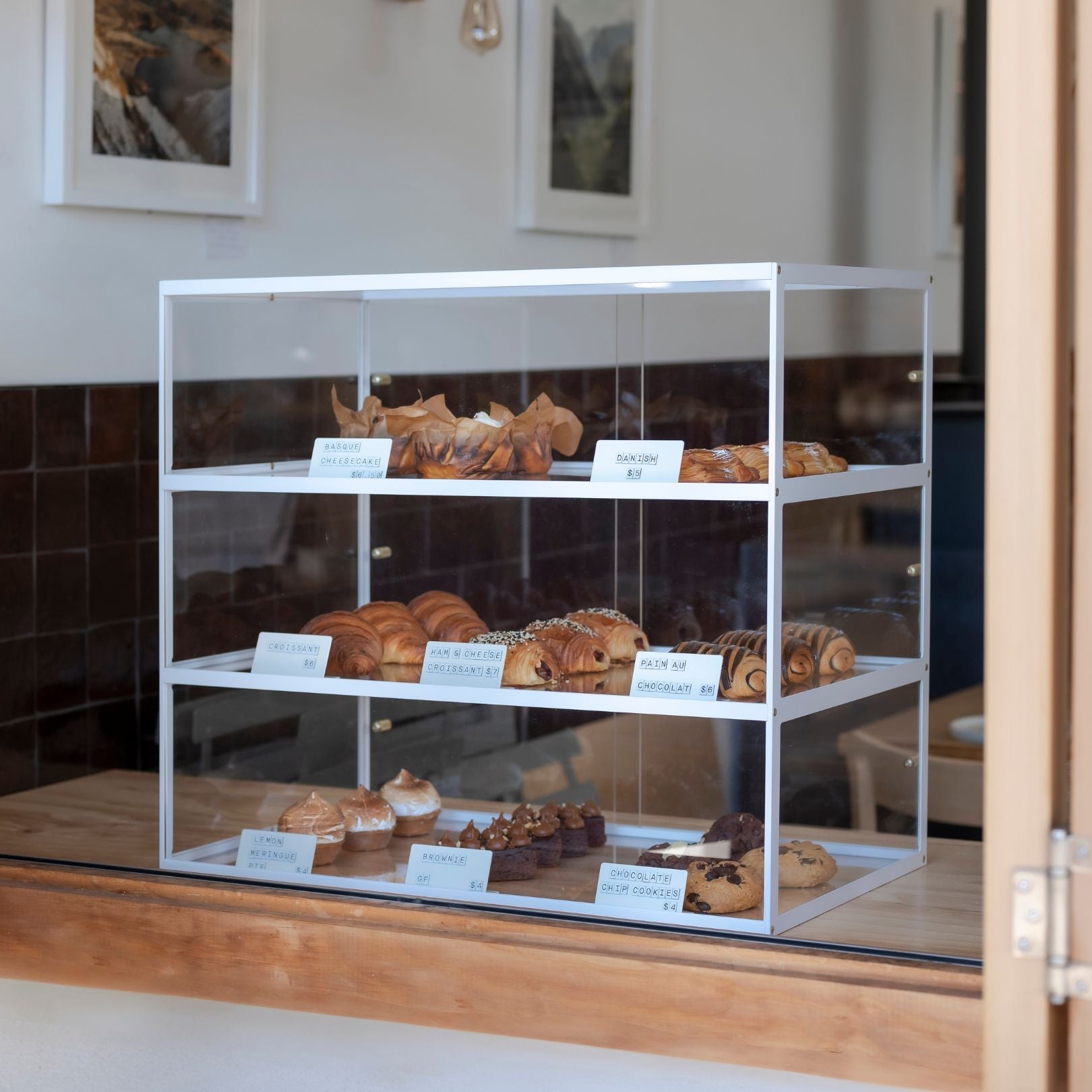 white three tier bakery display case with baked goods sitting at a cafe window