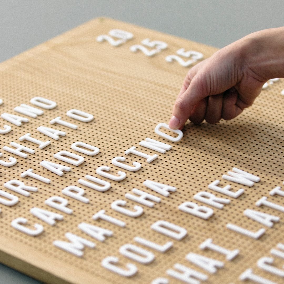 Close-up of hand placing white peg letters onto oak wooden peg letter board
