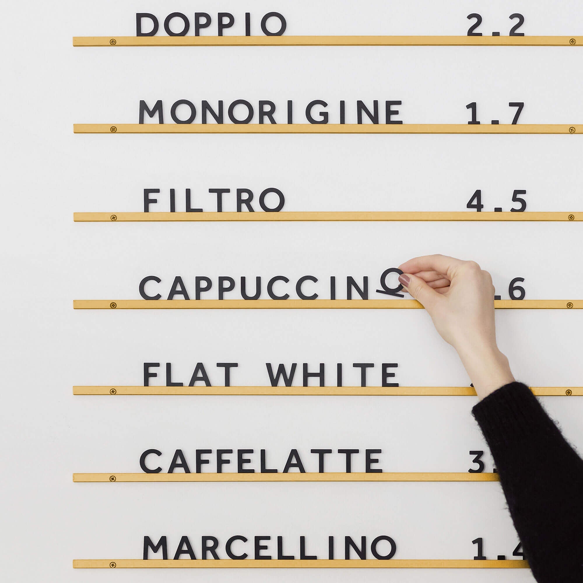Atelier Letter Board in brass finished rails with café menu, with a hand adjusting black letters spelling cappuccino