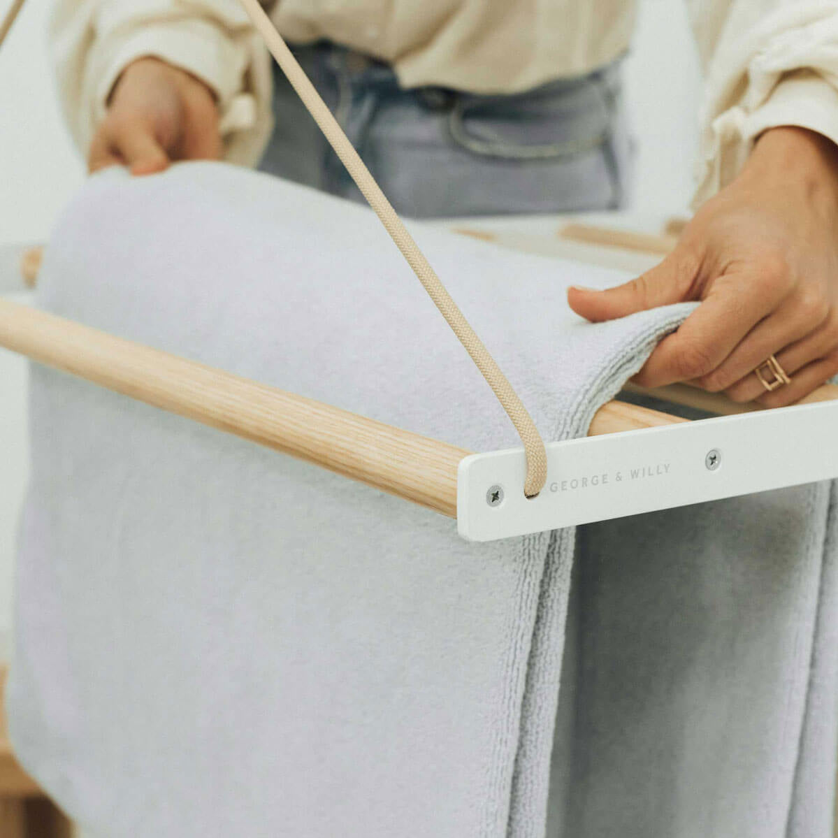 close up of person adjusting clothes on dowels of ceiling hanging drying rack