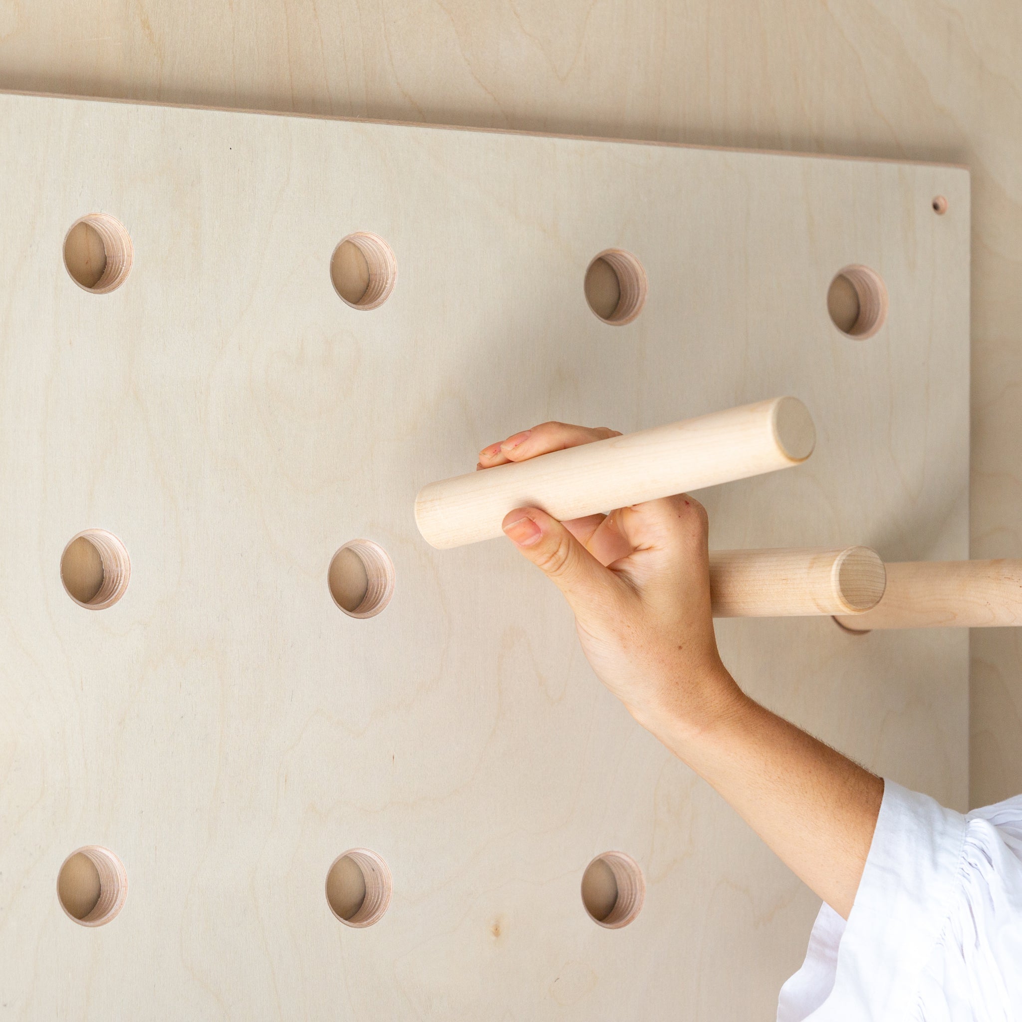 hand putting in a wooden peg to the holes of the wooden pegboard shelf
