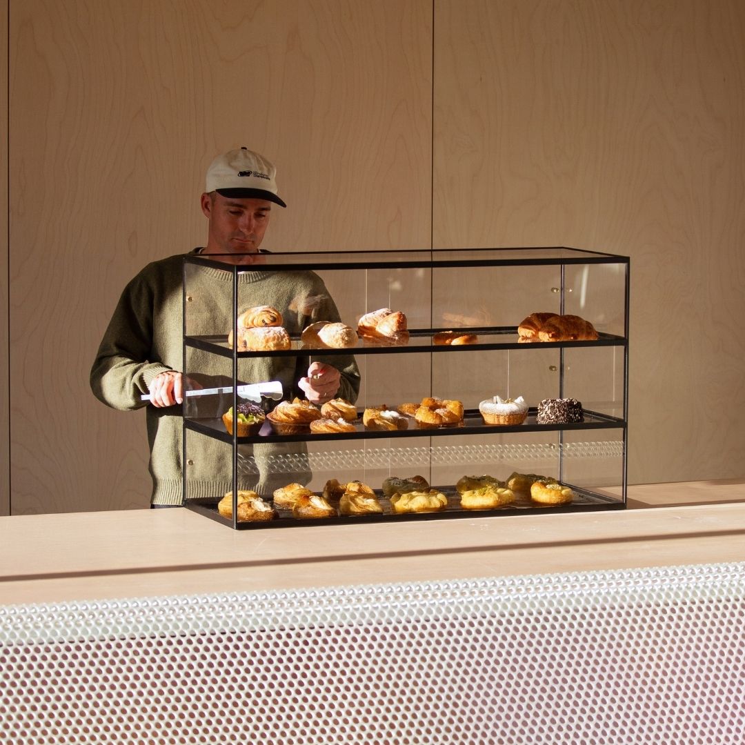 black three-tier bakery display case filled with pastries on a countertop with boy reaching into it