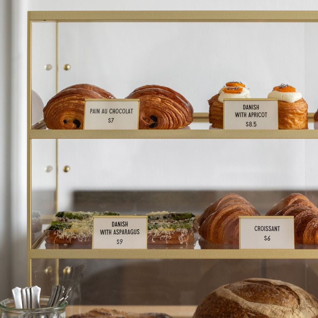 close up of brass acrylic glass display cabinet for bakeries and collectables full of pastries with signs displaying names