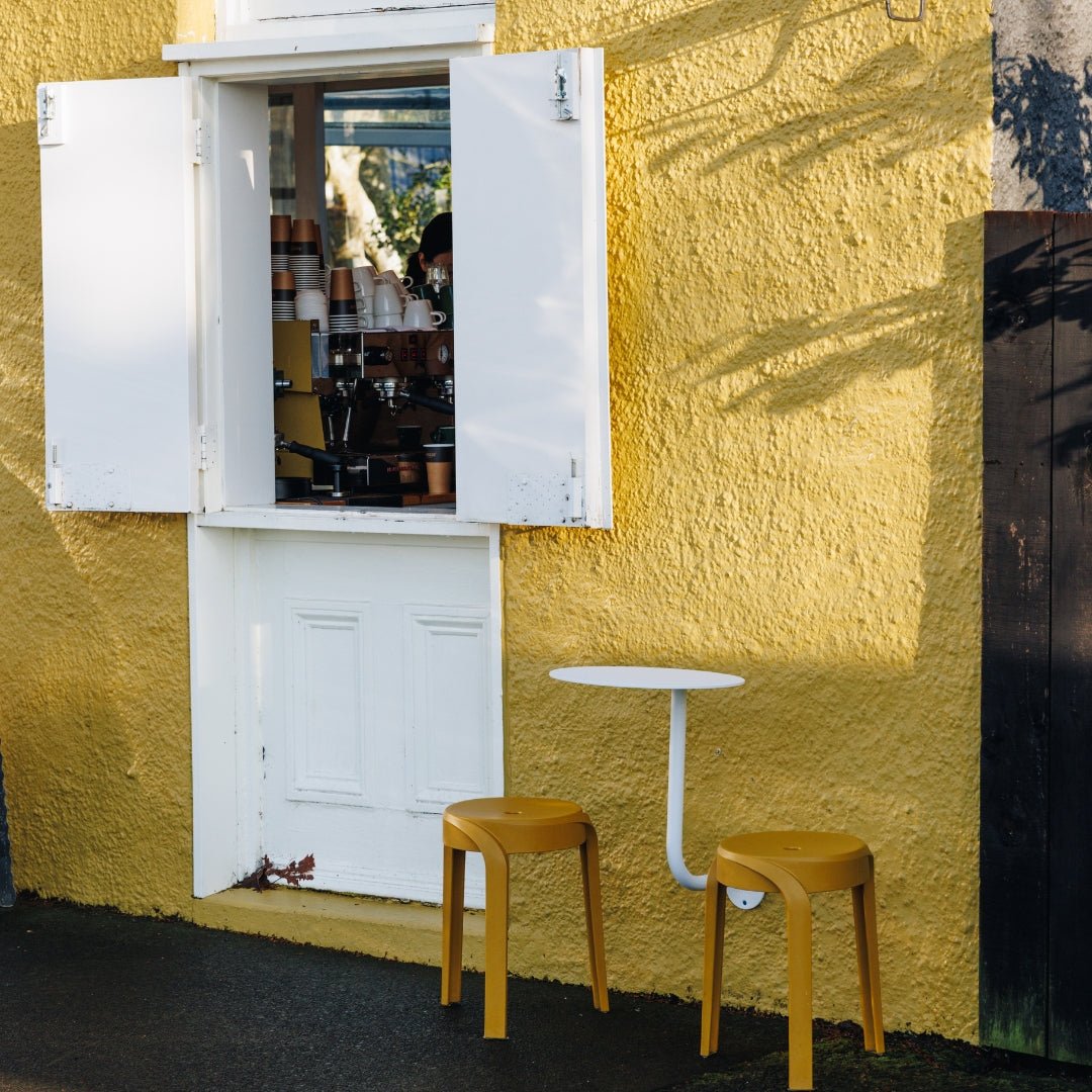 white wall mounted cafe table installed outside a yellow coffee kiosk window front