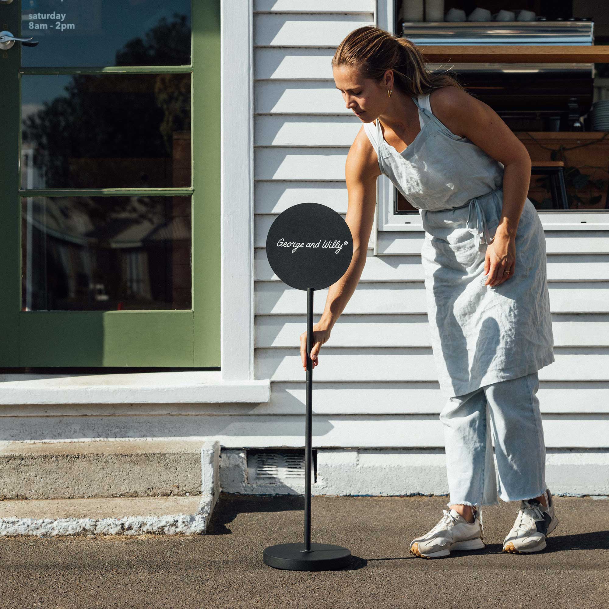 black metal freestanding round advertising sign with logo being placed on pavement by person