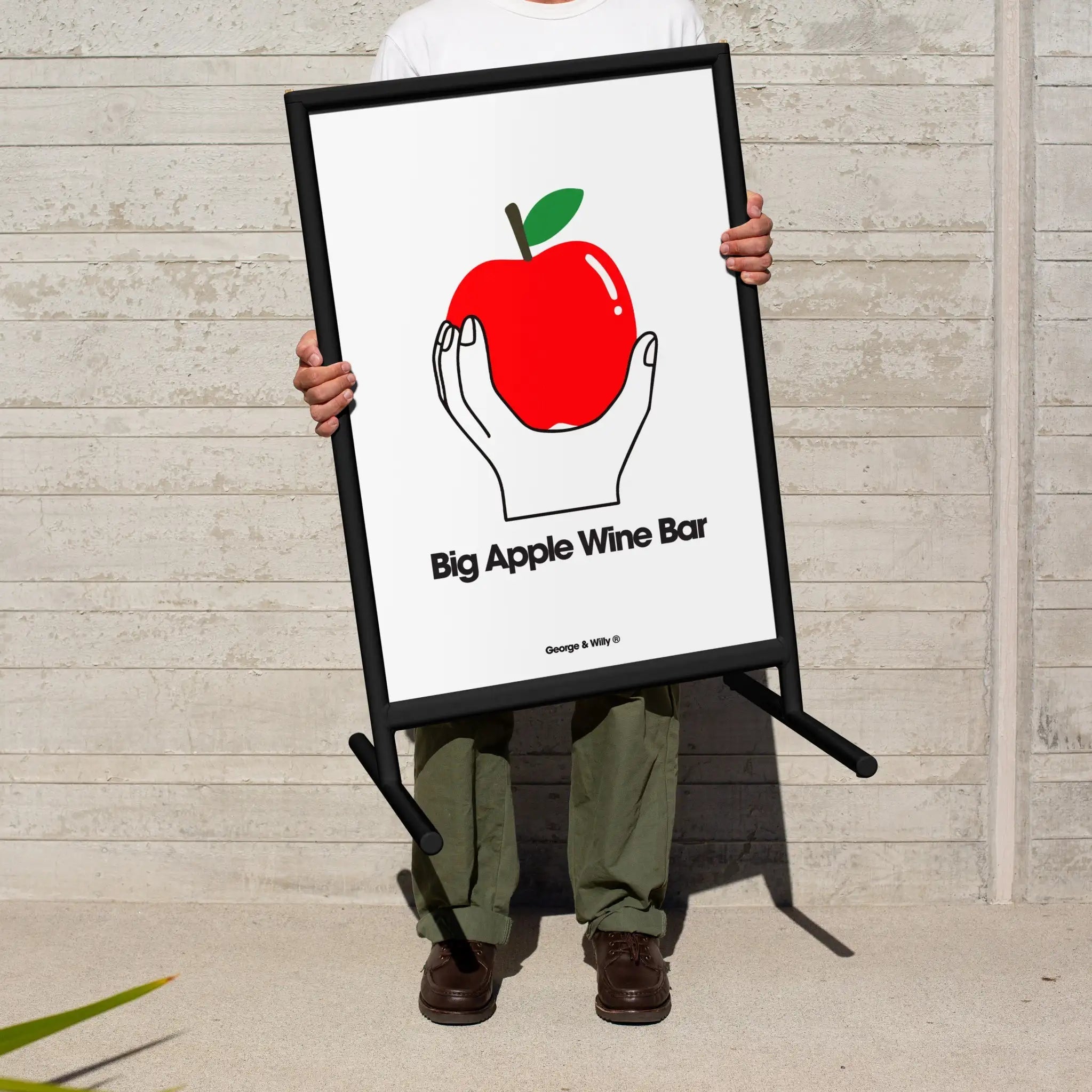 person holding up black framed poster sidewalk sign with a poster of an apple inside