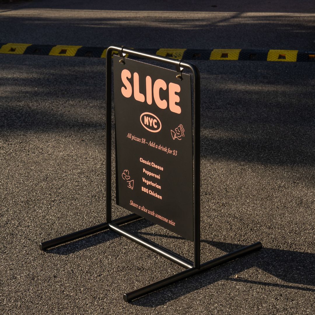 side angle profile of black metal swing business sign with golden hour light on the branding decal outside on pavement