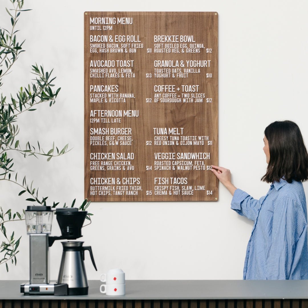 Large wooden peg letter board in walnut finish mounted on wall, showing menu layout in café setting