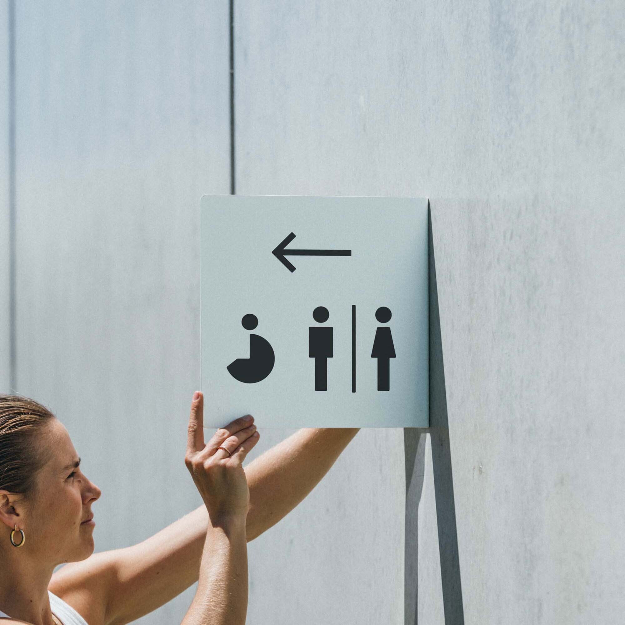 girl installing the larger sized square blade sign with bathroom decals on it